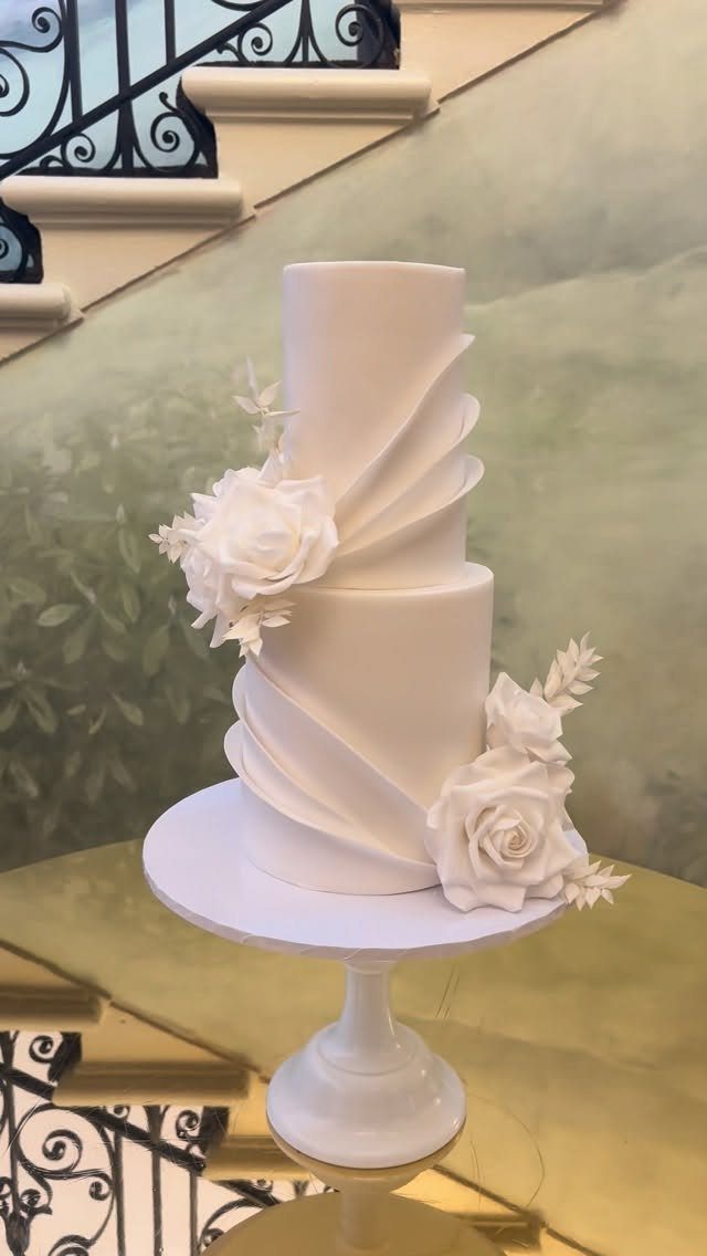 37 Wedding Cakes with Flowers to Inspire Your Design 34 Three-tier white wedding cake decorated with white sugar roses on a white stand.
