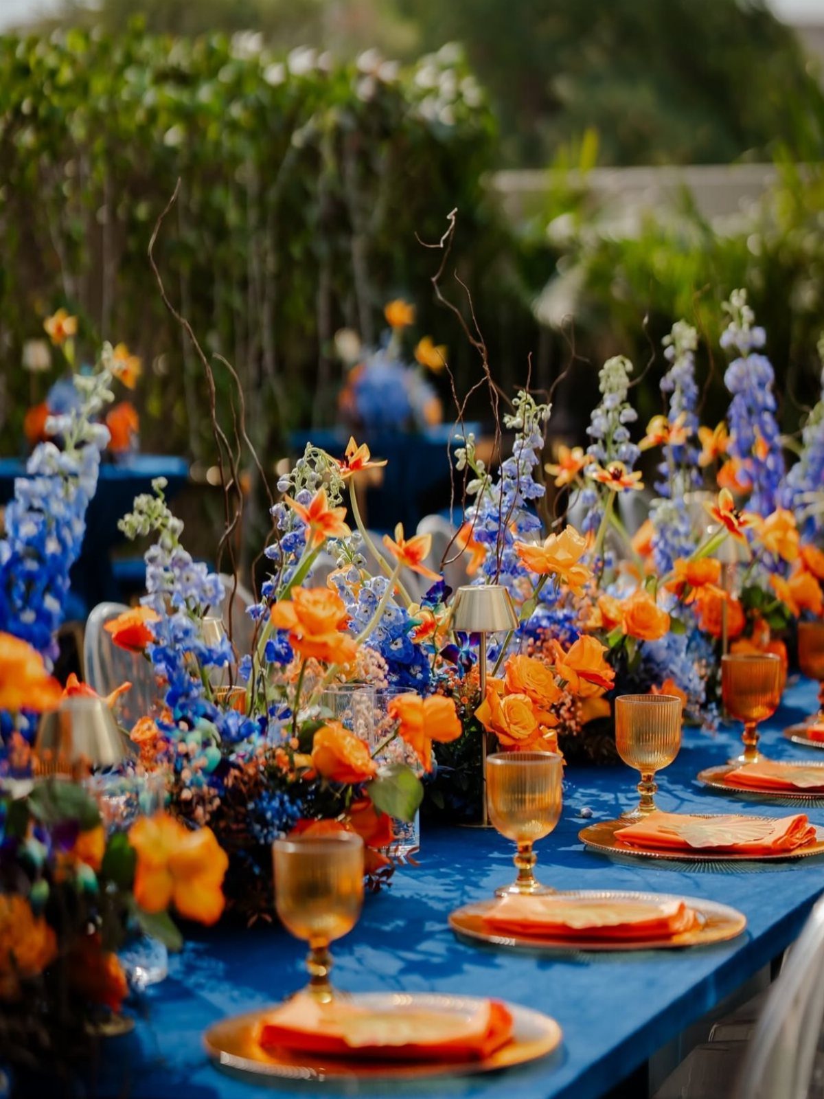 Blue and orange wedding table setting with matching floral arrangements and orange glassware.