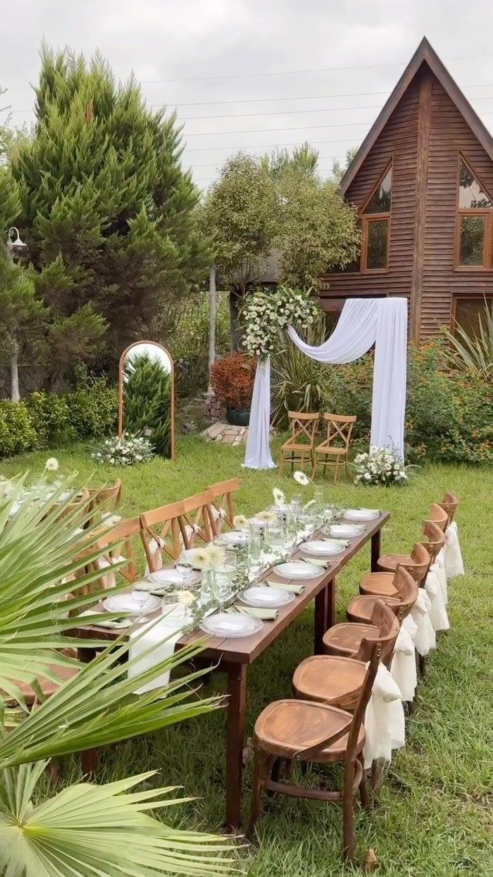 Long wooden wedding table set for guests in a garden by a cabin