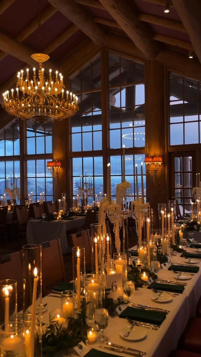 Formal dining table with many lit candles and a gold chandelier in rustic room