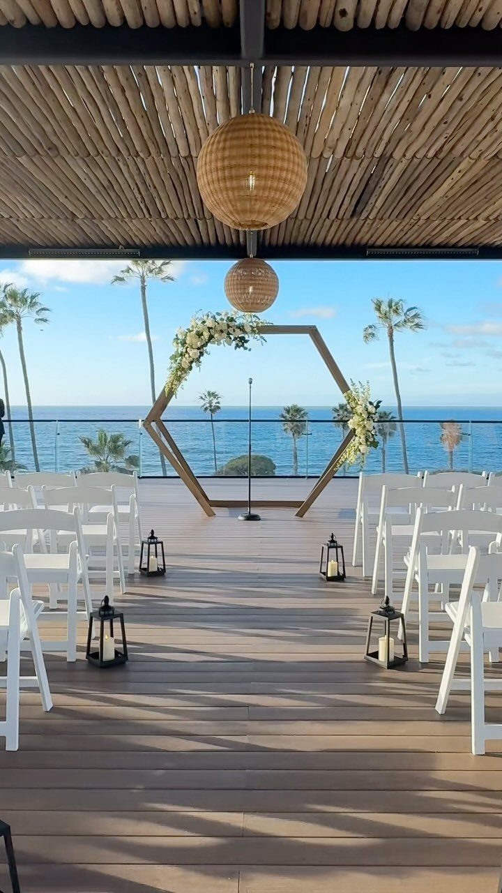 Wedding ceremony setup with white chairs and hexagonal arch overlooking a tropical beach.