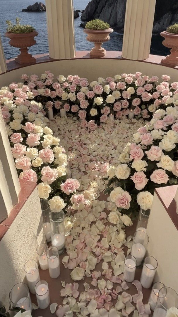 Heart-shaped rose petal arrangement with white candles on a terrace overlooking the ocean.