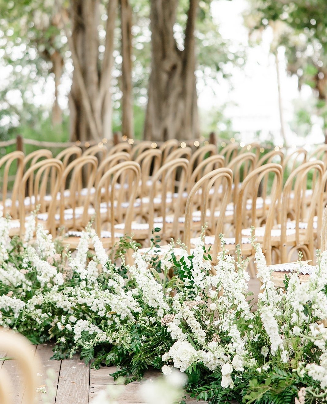Wooden ceremony chairs with a white floral border in an outdoor garden setting