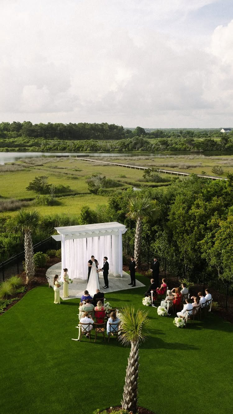 Outdoor wedding ceremony with a small guest list under a white pergola by a marsh.