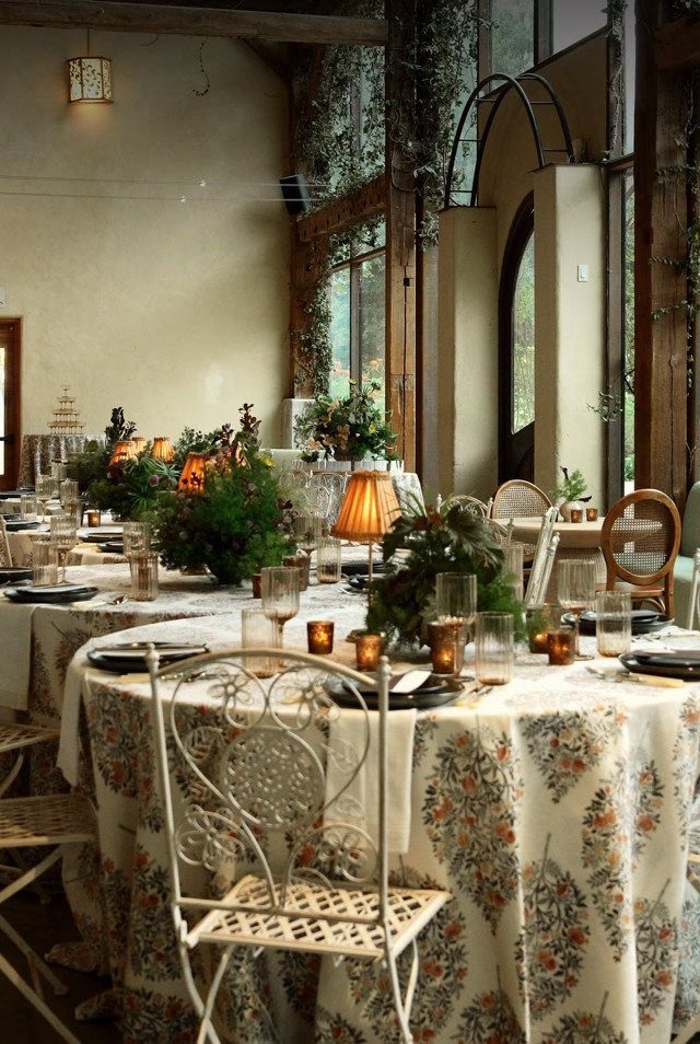 Floral tablecloth and ornate white chairs at a wedding reception table with greenery.