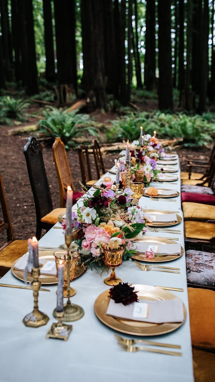 Long wedding table with gold plates and floral centerpieces in a redwood forest