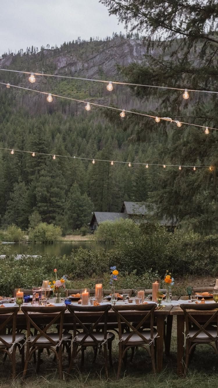 Outdoor dining table with candles and string lights set against a mountain forest landscape