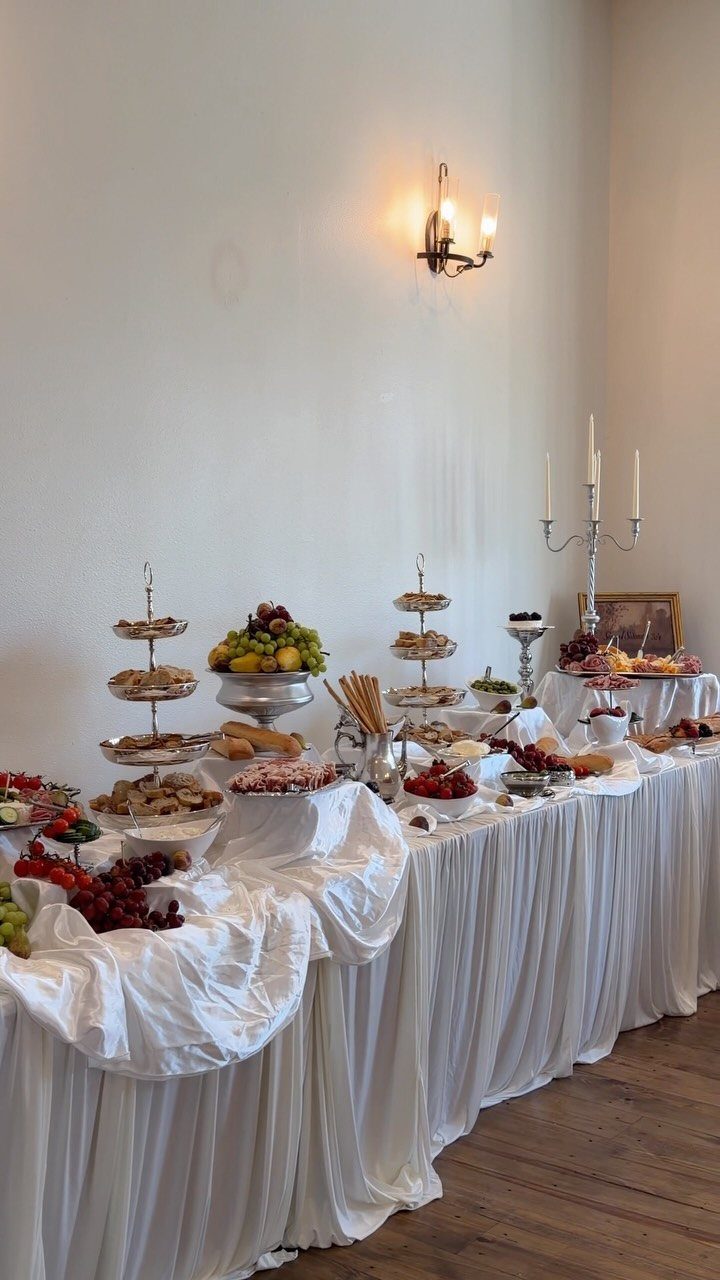 Buffet table with white linens featuring a variety of charcuterie, fruits, and appetizers.