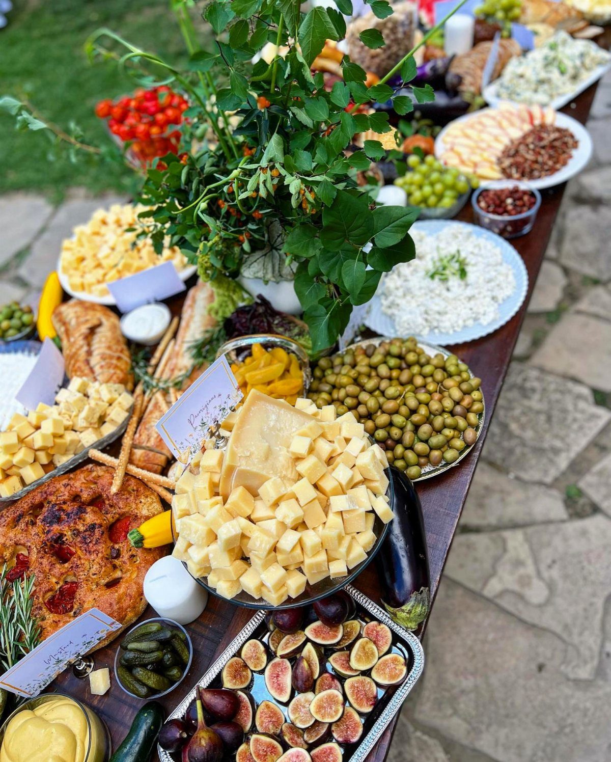 Abundant grazing table with cheeses, olives, figs, and greenery for a wedding event.