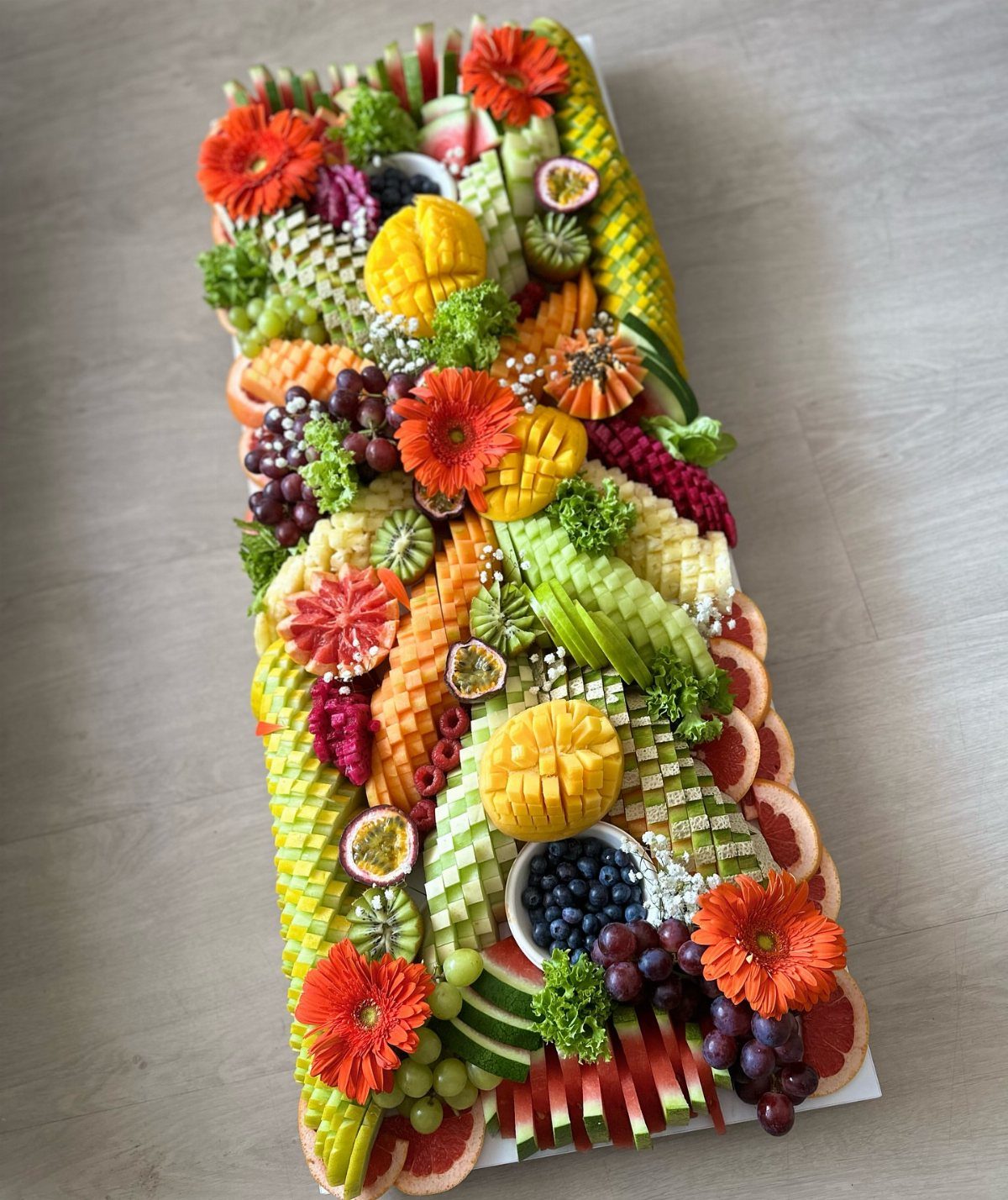 Colorful fruit and vegetable grazing platter decorated with orange flowers and fresh greenery.