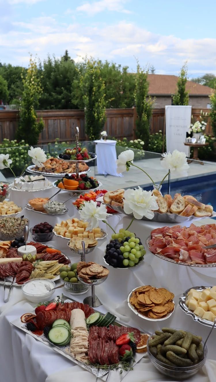 Outdoor grazing table with meats, cheeses, and white flowers by a swimming pool