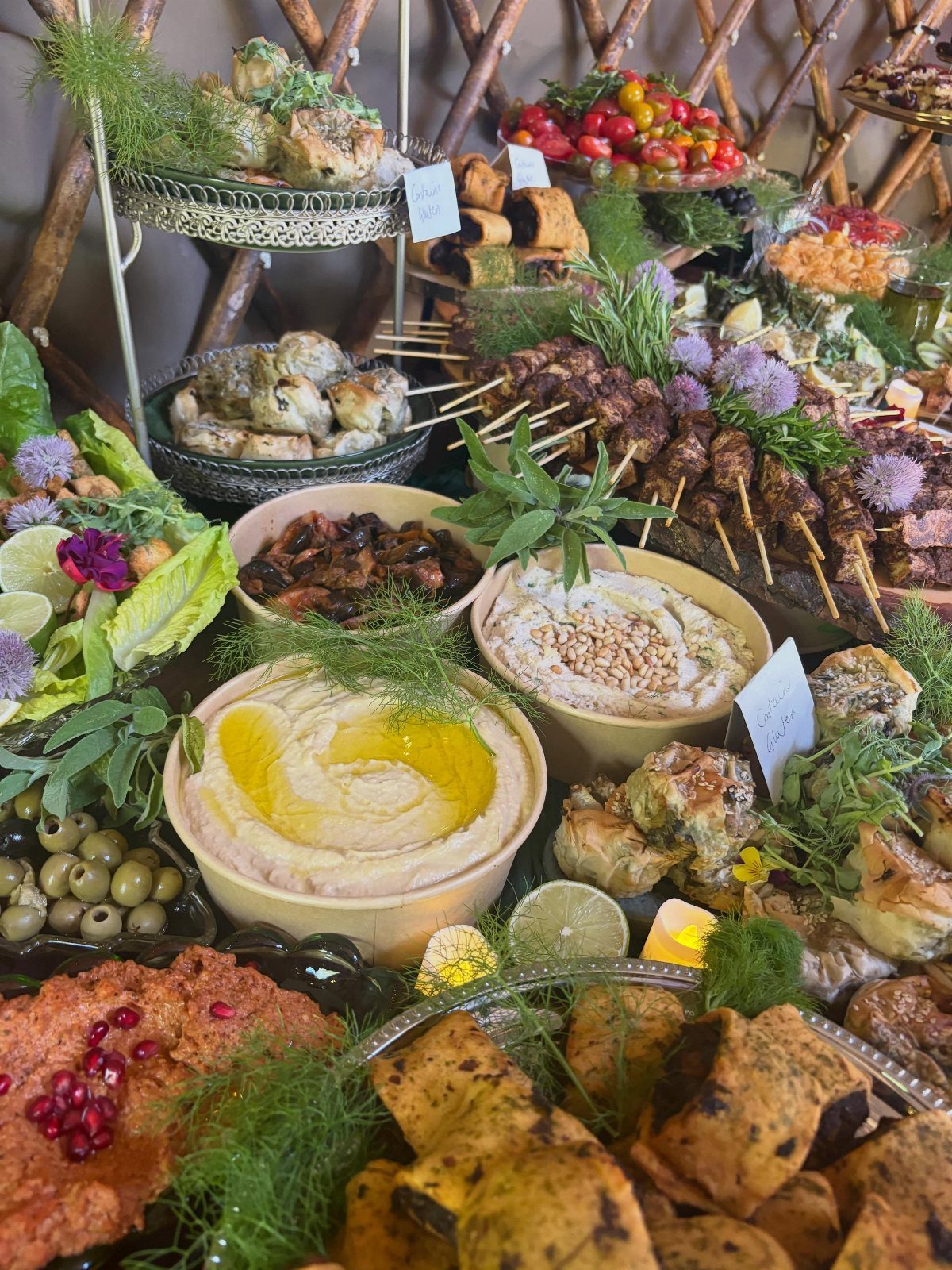 Mediterranean grazing table with hummus, grilled skewers, olives, and stuffed grape leaves.