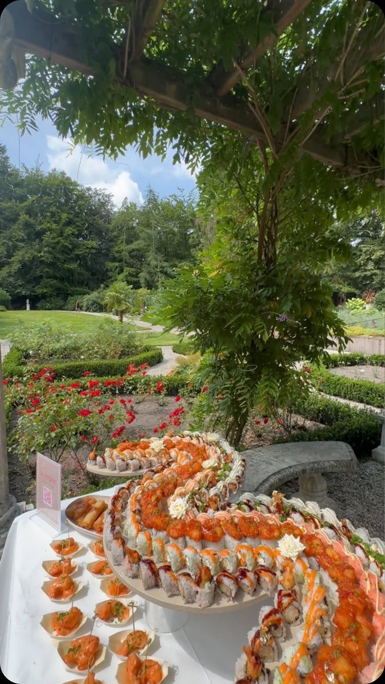 Sushi grazing table with a winding arrangement of rolls and sashimi in a garden.