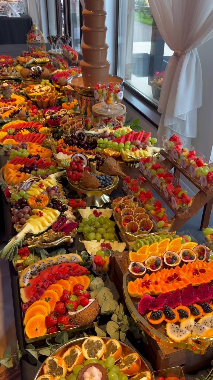 Tropical grazing table with sliced exotic fruits, berries, and a chocolate fountain.