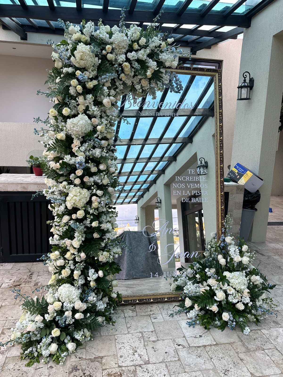 Wedding Mood Board Ideas: 39 Styles from Celestial to Coastal 16 Gold-framed mirror decorated with white floral arrangements on a stone patio.