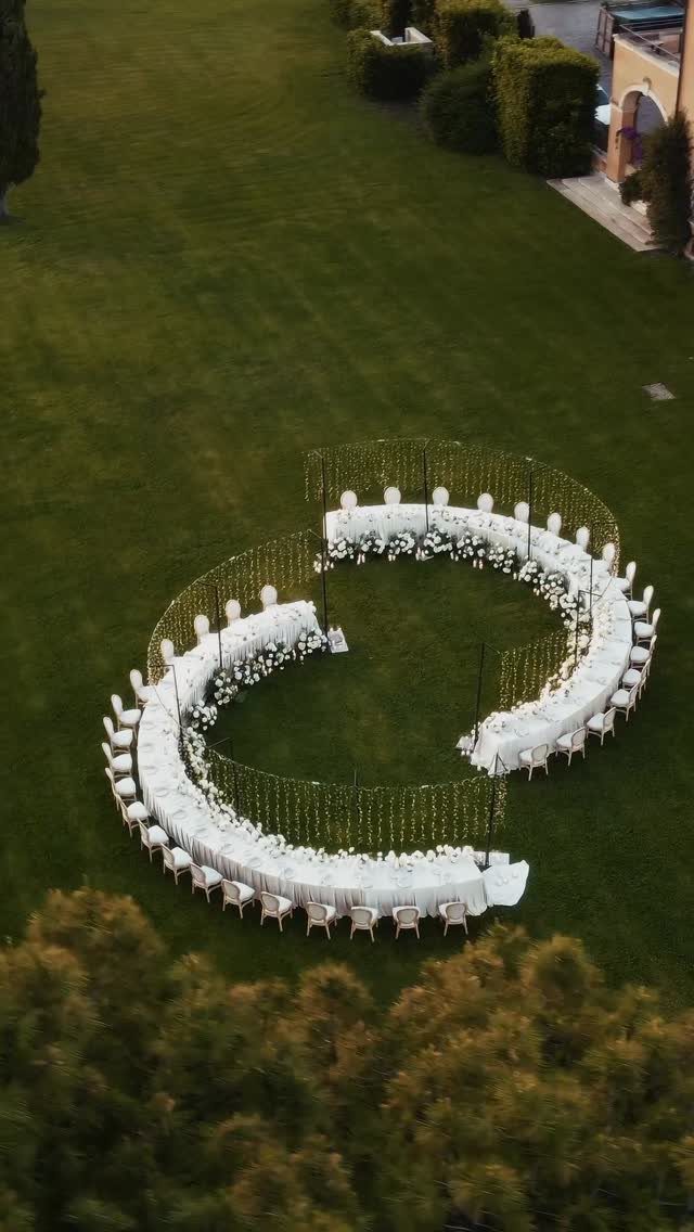 Wedding Mood Board Ideas: 39 Styles from Celestial to Coastal 31 Curved white dining tables and chairs arranged in a spiral on a green lawn.
