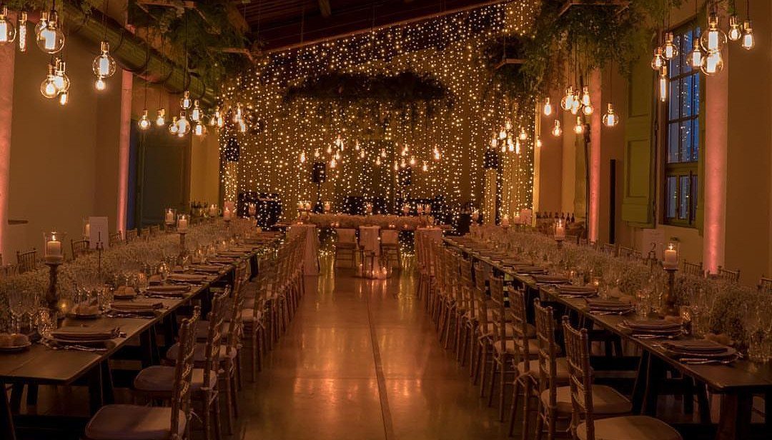 Wedding Mood Board Ideas: 39 Styles from Celestial to Coastal 9 Vintage-style bulbs and fairy lights hanging over long dinner tables in a wedding venue.