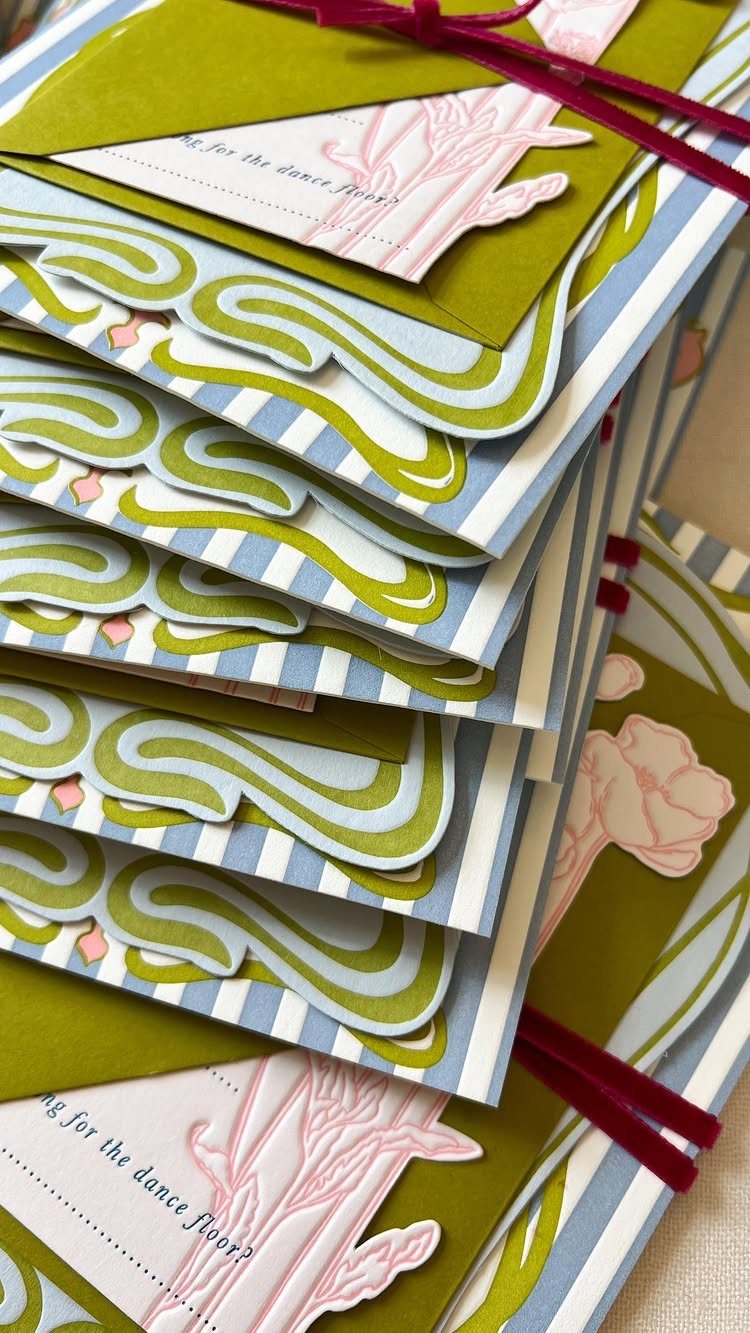 Stacked wedding invitations with olive green, blue stripes, and Art Nouveau swirling designs.