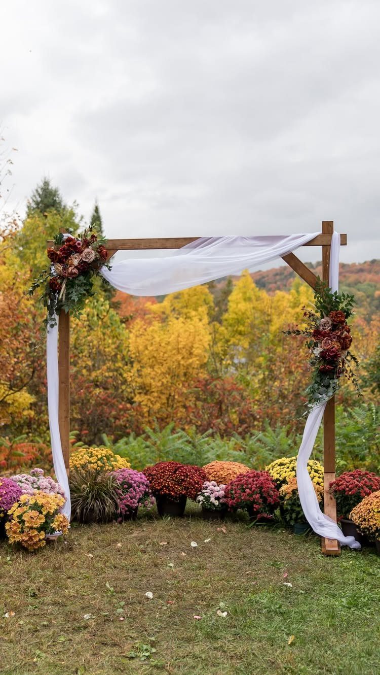 Wooden wedding arch with white fabric and red flowers against autumn foliage.
