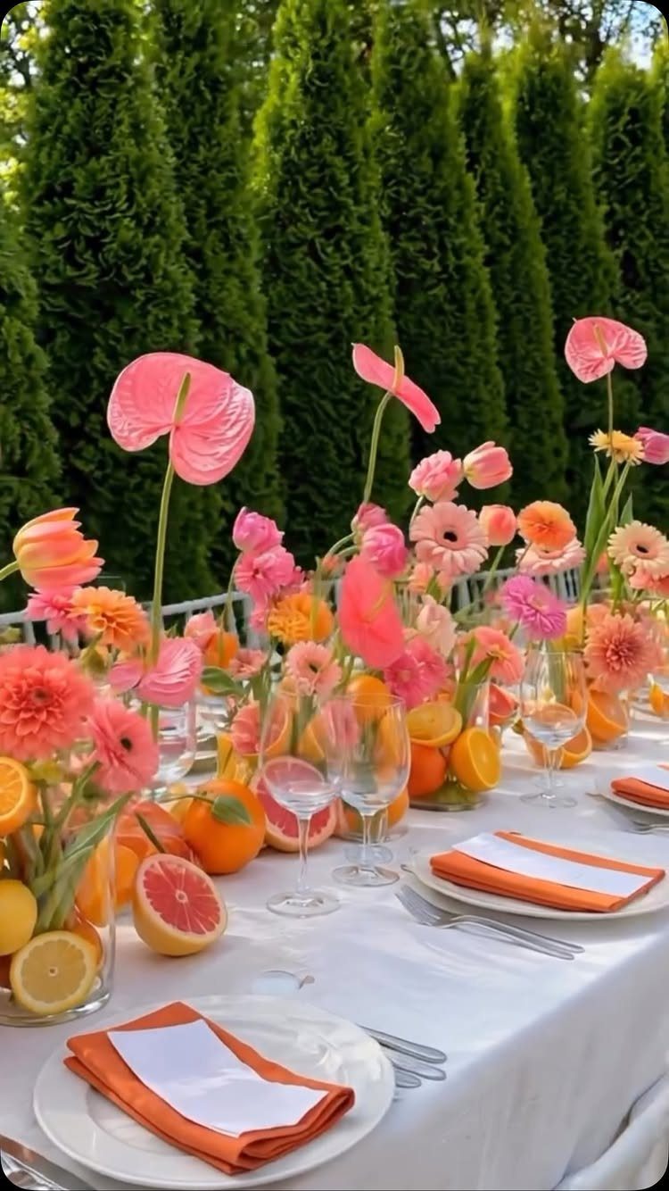 Orange and pink floral centerpieces with citrus fruits on a white wedding table.