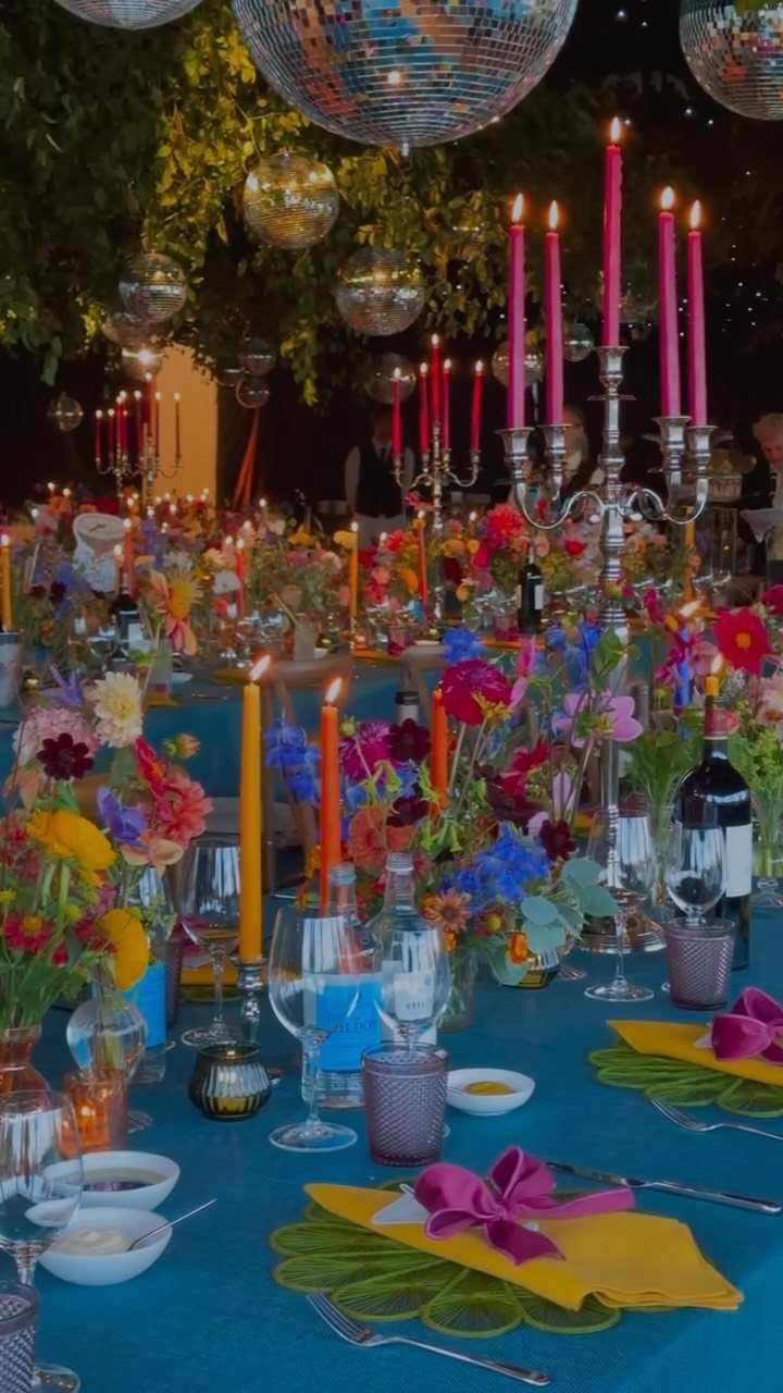 Colorful wedding table setting with blue cloth, vibrant flowers, and pink candles.