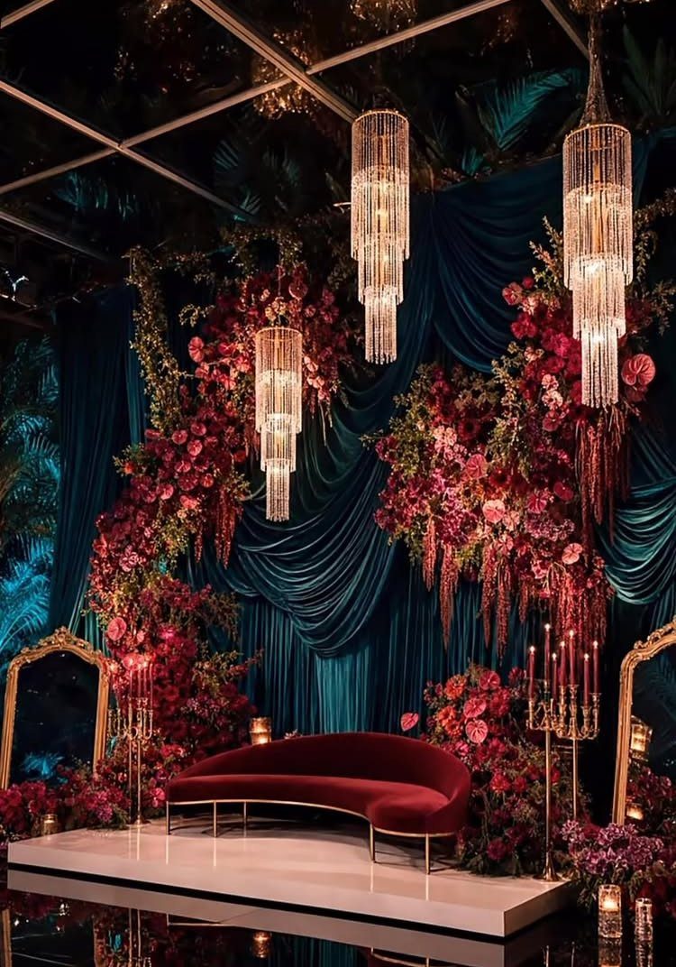 Emerald green draped backdrop with red flowers, crystal chandeliers, and a red velvet sofa.
