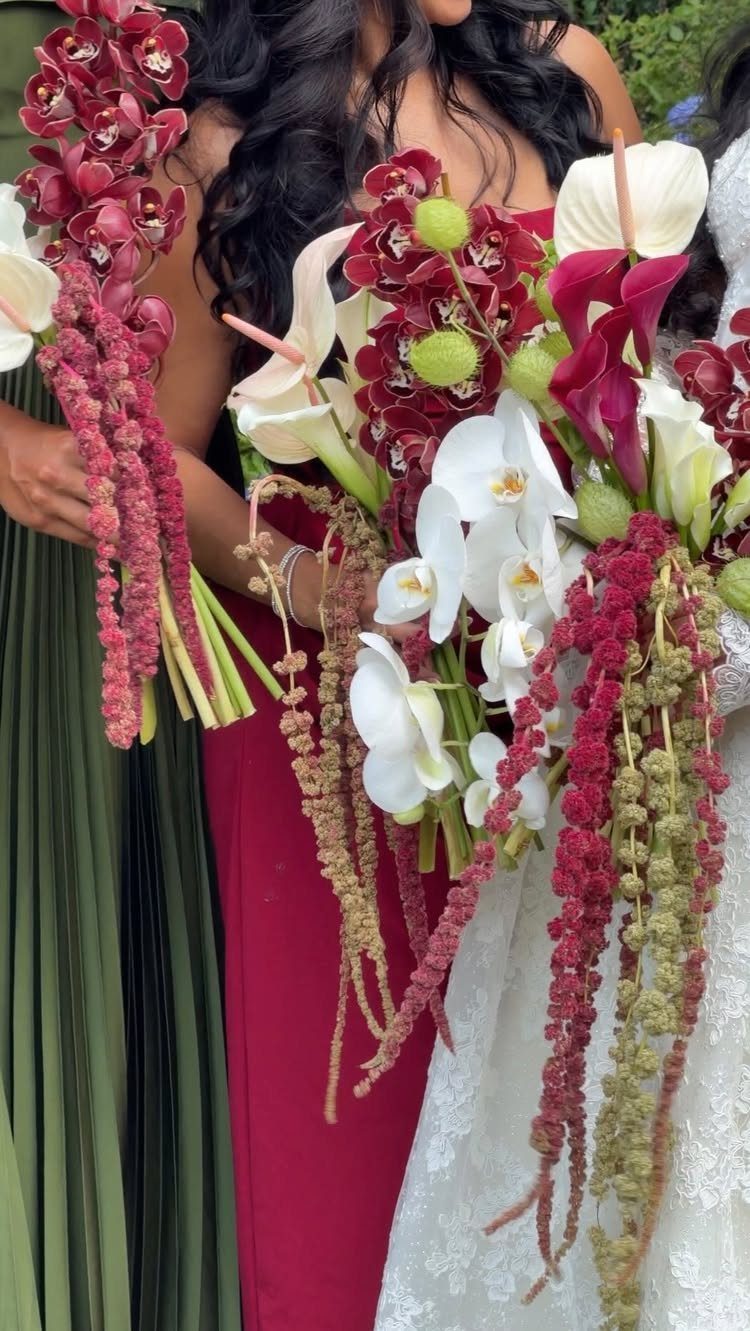 Bridesmaids in olive green and red dresses holding lush red and white bouquets.