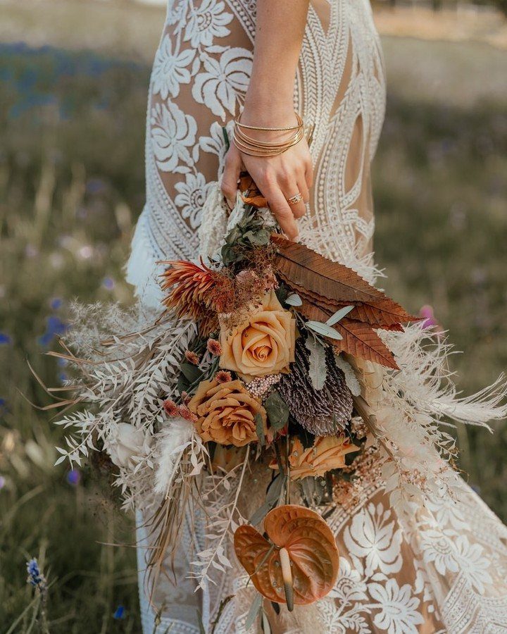 Bridal bouquet with orange roses and dried foliage held by a lace-clad bride.