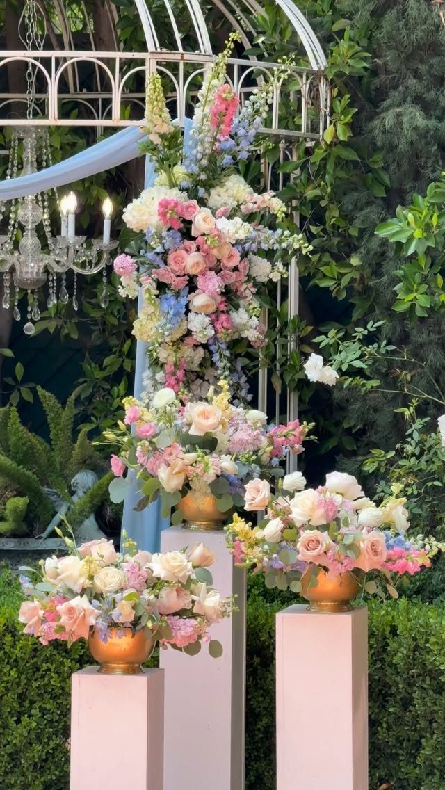 Pastel pink and blue floral arrangements on pink pedestals under a white gazebo.