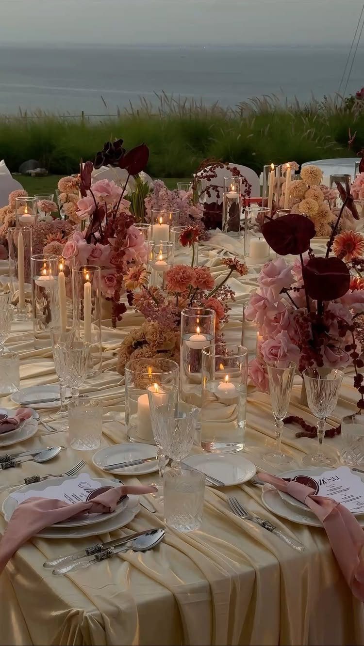 Champagne gold wedding table with pink and burgundy flowers and glowing candles.