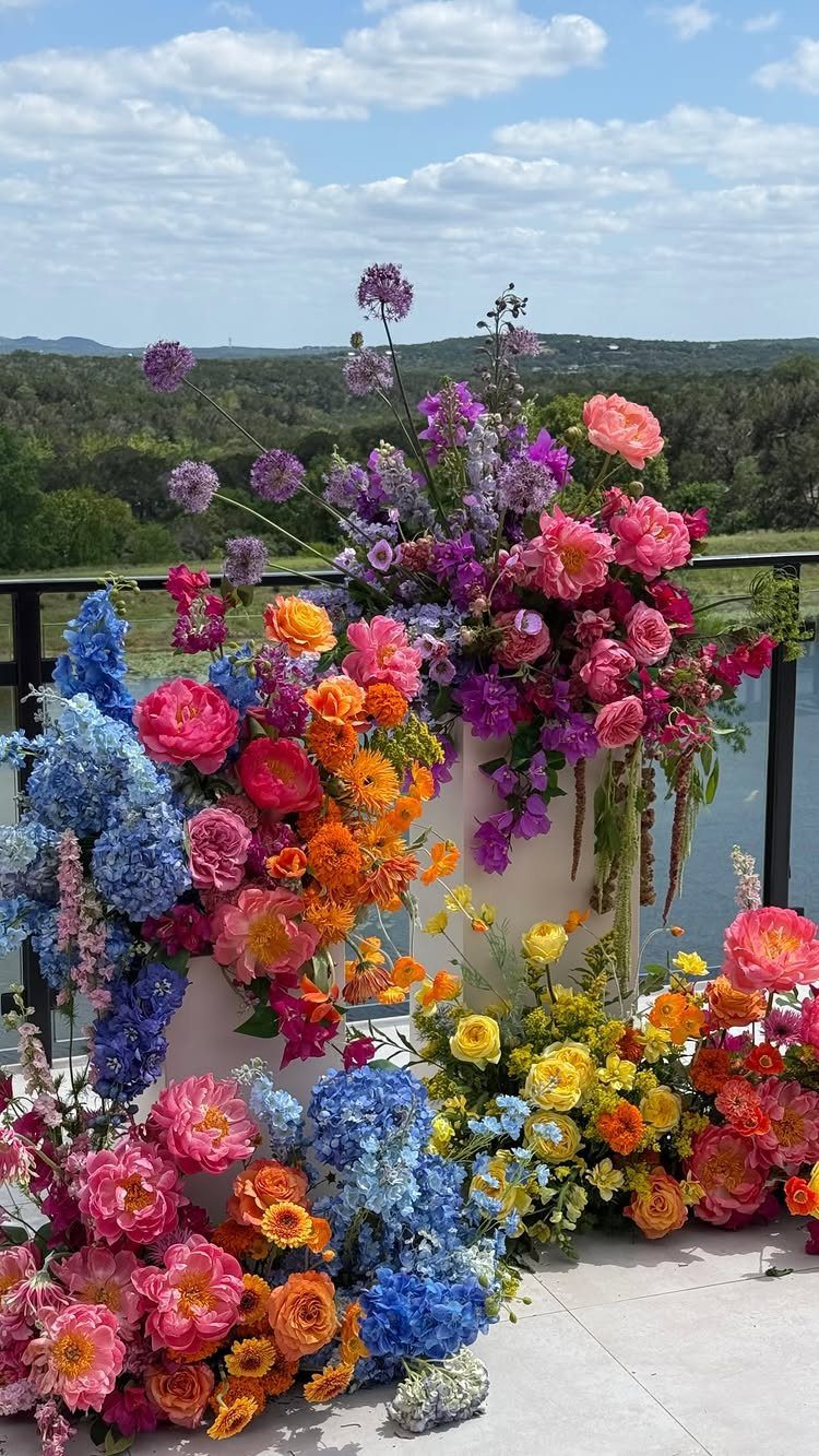 Colorful floral arrangement with pink, orange, and blue flowers on an outdoor balcony.