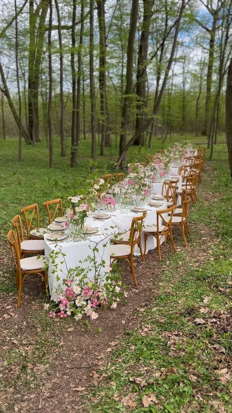 Long white wedding table with pink flowers set in a lush green forest